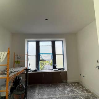 Room with a bay window skim-coated and painted, masked off mid-renovation