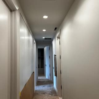 Narrow hallway repainted in clean white with new recessed lighting and trim